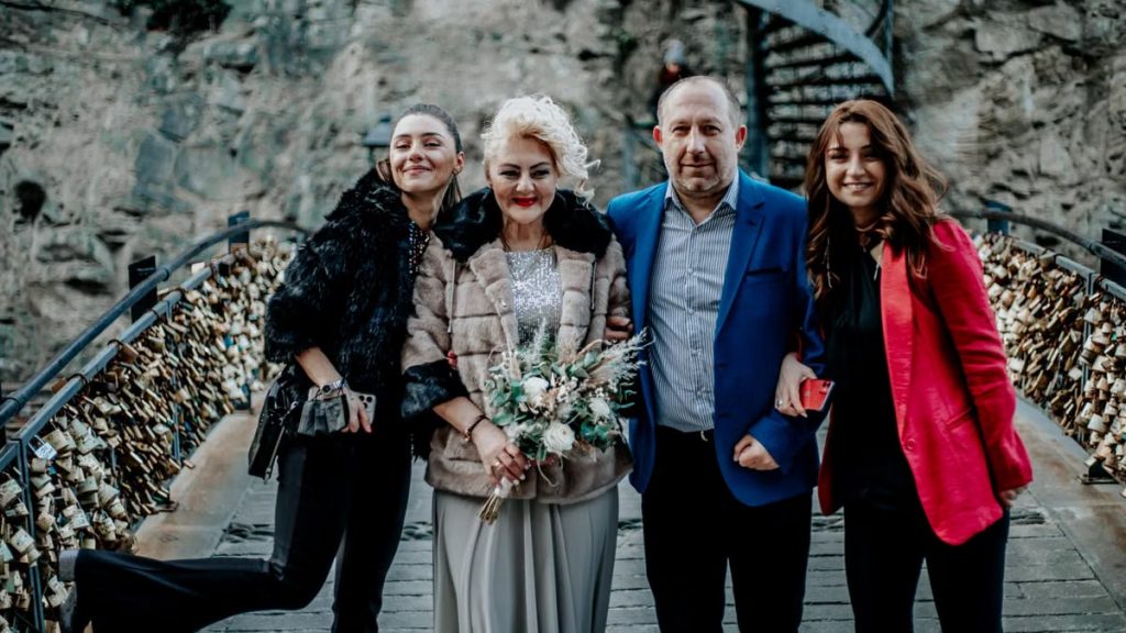 A joyful family in formal attire standing together on a bridge with love locks.